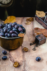 fresh plums in vintage metal pan with old keys, vintage wooden box and dry leaves on brown gradient background