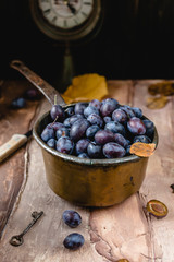 fresh plums in old metal pot on brown gradient background with dry leaves