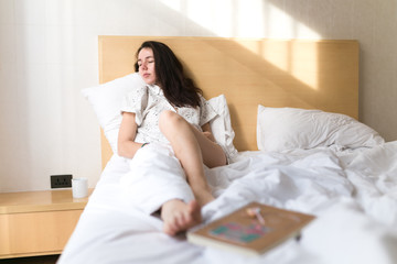 Brunette girl, young women on bed with cup of coffee and notebook.  Lazy morning in hotel