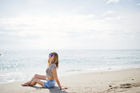 Beautiful model relaxing on a beach of sea, wearing on jeans short, leopard shirt and sunglasses.