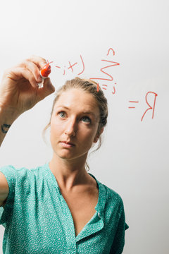 Young woman writing complex equation onto glass wall