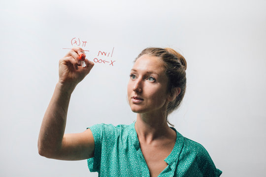 Young woman writing complex equation onto glass wall