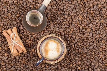 A cup of freshly brewed coffee, pot and cinnamon on coffee beans