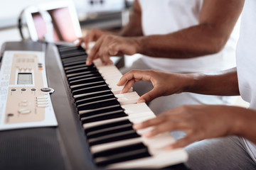 Obraz premium Close up. A black man sits in the living room of his apartment and plays a synthesizer. A girl is sitting next to him.