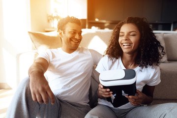 Black man and woman are sitting on the couch. A man and a woman hold a helmet of vr in their hands and dispose of it.