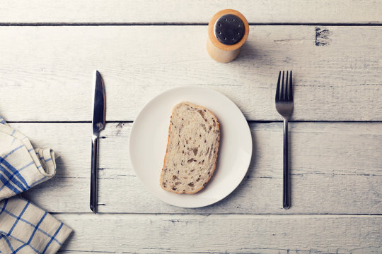 poor lunch - slice of bread on a plate and cutlery on wooden table