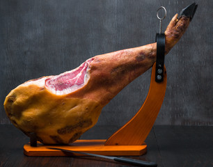 Whole mediterranean traditional jamon on a wooden stand with a knife lean on a table. Dark image