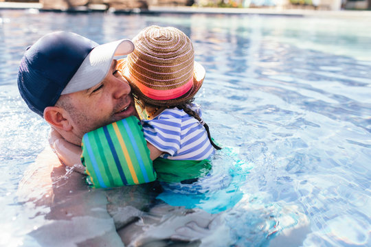 Father and daughter in outdoor swimming pool, daughter hugging father