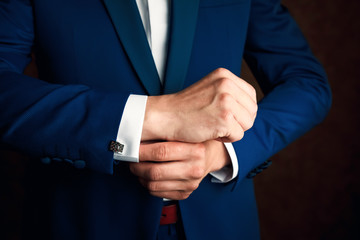 A man in a blue suit straightens his sleeves