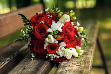 Gold wedding rings on a wooden bench on the background of a beautiful wedding bouquet