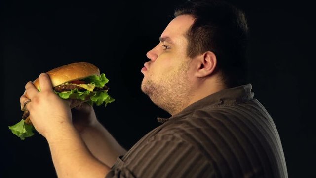 Fat man eating hamberger fast food . Breakfast for overweight person . Junk meal leads to obesity. Person regularly overeats concept .