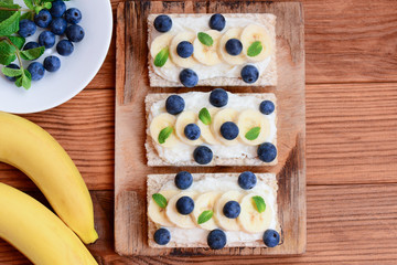 Cottage cheese, fresh bananas and berries sandwiches with crisp bread on wooden board. Vegetarian sandwiches recipe. Top view