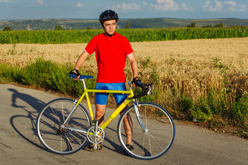 Obraz premium Sportsman standing next to bicycle. Wearing sports gear, helmet and glasses. Natural background.