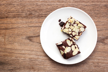 Brownie sliced with almond sliced topping on white plate. Top view over wooden table.