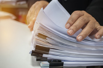 Businessman hands working in Stacks of paper files for searching information on work desk office, business report papers,piles of unfinished documents achieves with clips indoor,Business concept