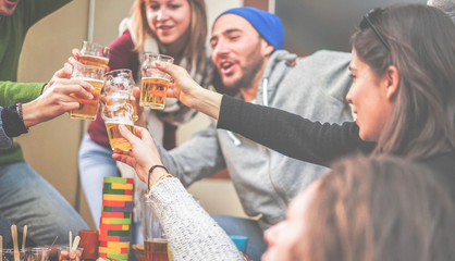 Happy friends cheering with beer and playing board games in bar pub restaurant - Young people toasting appetizer in brewery chalet - Concept about good and positive mood - Focus on left bottom hand