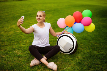 A woman is sitting on the grass. Near the monoclean, to which the inflatable balls are attached.