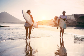 Surfers couple running with surf boards on the beach  - obrazy, fototapety, plakaty