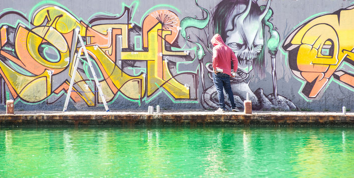 Tattoo graffiti writer finishing his paint in urban river contest 