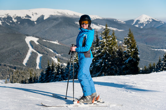 Happy female skier resting on the top of the mountain at ski resort, wearing blue ski suit, mask and black helmet snow happiness enjoyment activity recreation winter seasonal sports concept