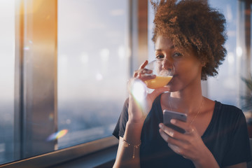 Dainty young African American curly female sitting alone in restaurant next to window and drink...