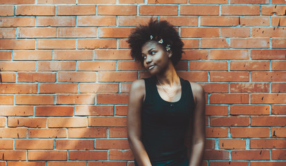 Lovable black young female in front of brick pattern background on summer day looking aside;...