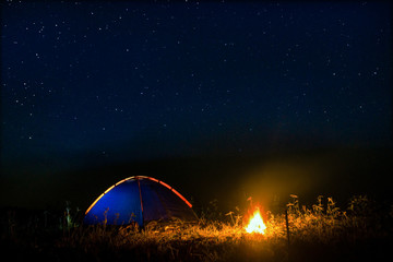 Night camping. campfire near illuminated tent under amazing night sky full of stars