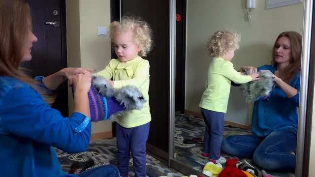 Happy family girls measuring warm winter hats near mirror