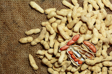 stack of peanuts and peeled peanuts on  old brown hemp sack