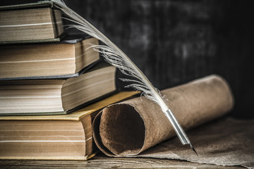 Old quill pen with old paper scroll and books on the table. Letter writing. Historical atmosphere. 