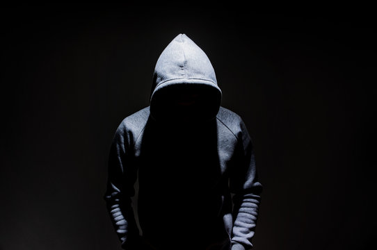 Silhouette of man in the hood, dark mysterious man hoodie, murderer, hacker, anonymus on the black background with free space
