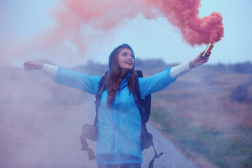 Young traveler woman wearing a raincoat and holding smoke bomb in hand