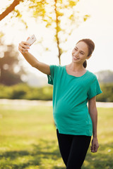 Fototapeta premium Pregnant woman doing selfie in the park on her smartphone