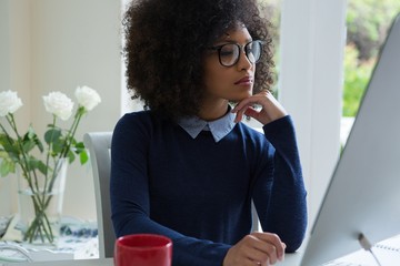 Thoughtful woman working on desktop pc at desk