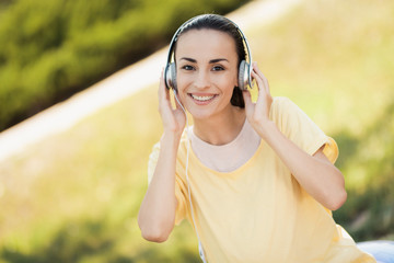 Pregnant woman in a yellow T-shirt sits on a ball for yoga and listens to music