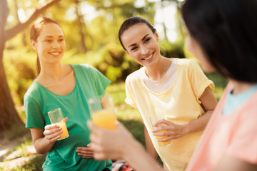 Three pregnant women sit in the park after practicing yoga and drink juice. They are resting