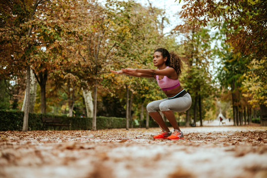 Hispanic girl doing squats in autumn park.