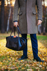 Clous up of the man in a coat and a leather bag in the beautiful autumn wood