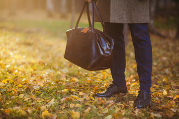Clous up of the man in a coat and a leather bag in the beautiful autumn wood