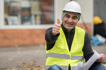 Smiling and successful construction worker posing showing thumbs up gesture. Outdoors