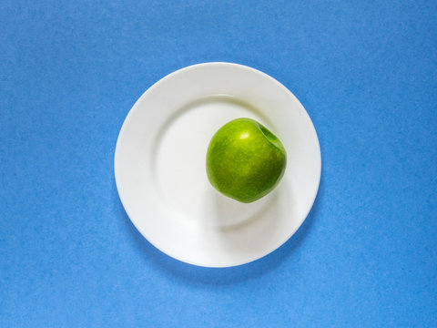 Green apple on a white plate. The view from the top. Blue background