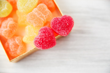 two red heart shape jelly candy in golden present box.white wooden table.space for text