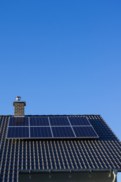 Brand new photovoltaics on house roof with chimney and blue sky