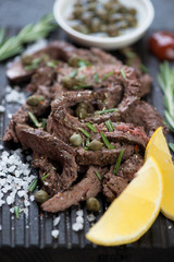 Close-up of beef tagliata with capers, fresh rosemary, olive oil and lemon. Selective focus, shallow depth of field