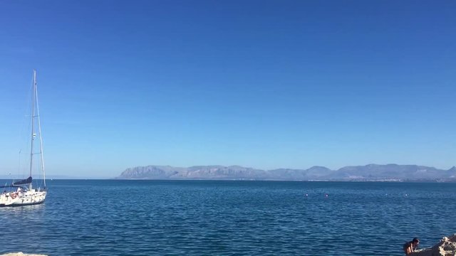 panoramic footage from scopello beach in sicily inside the zingaro national park with calm blue sea while a sailboat is moored off