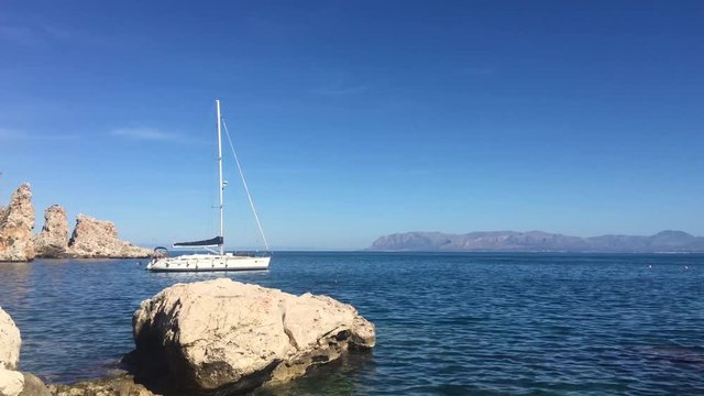 panoramic footage from scopello beach in sicily inside the zingaro national park with calm blue sea while a sailboat is moored off