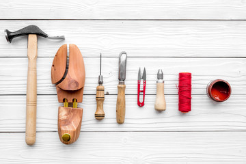 Shoe repair. Wooden last, hammer, awl, knife, thread on white wooden background top view pattern