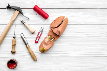 Shoe repair. Wooden last, hammer, awl, knife, thread on white wooden background top view copyspace
