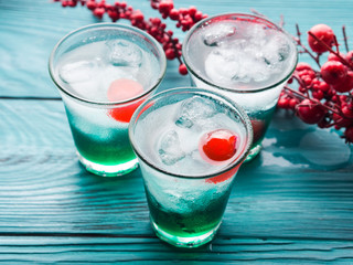 Christmas holiday party green alcohol drinks with cherry. Festive aperitif shots and ornaments on wooden dark table