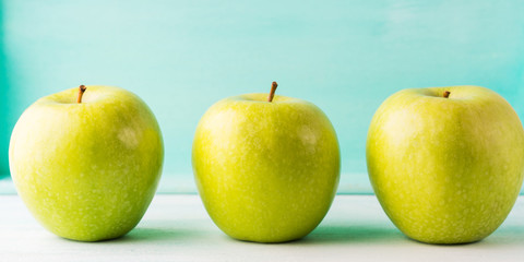 Three Green apples on turquoise background. Healthy food three pillars concept.